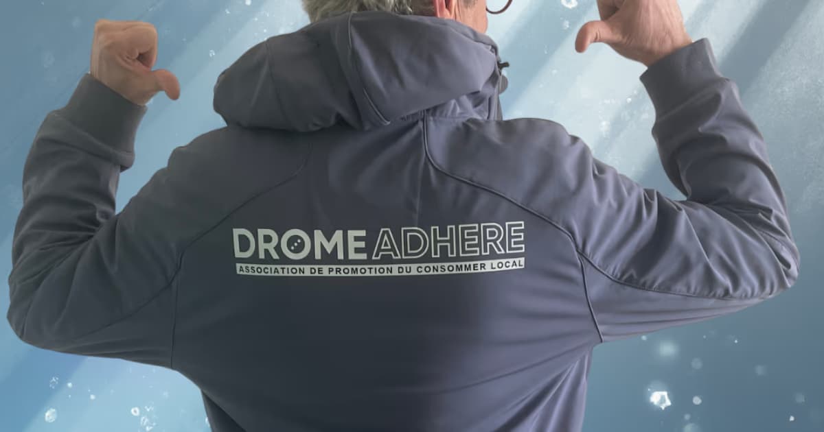 Un adhérent de dos, veste floquée DROMEADHERE, bras levés en signe de fierté.